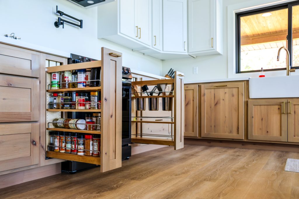 A modern kitchen showcasing custom wooden cabinets by Hostetler Custom Cabinetry, complete with two expertly crafted pull-out drawers designed for organized spice and utensil storage.